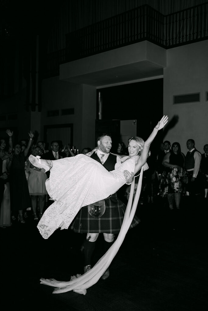 Guests lifting couple during lively wedding reception dance.