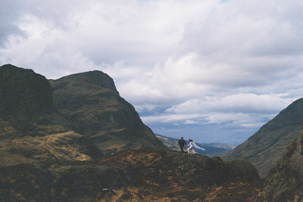 wedding couple walks across glencoe mountains in the distance