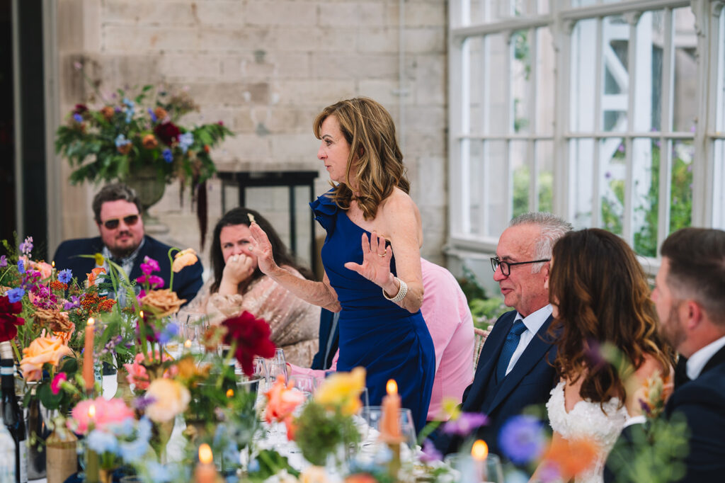 Woman giving speech at wedding reception while guests listen and smile.