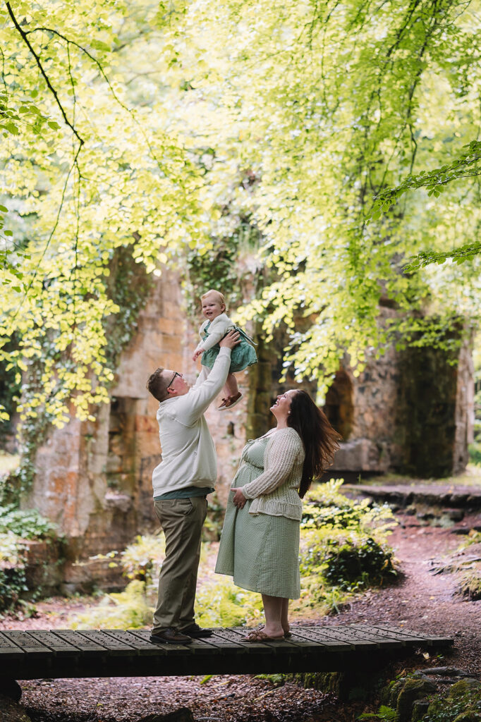 man throws laughing baby into the air while wife watches