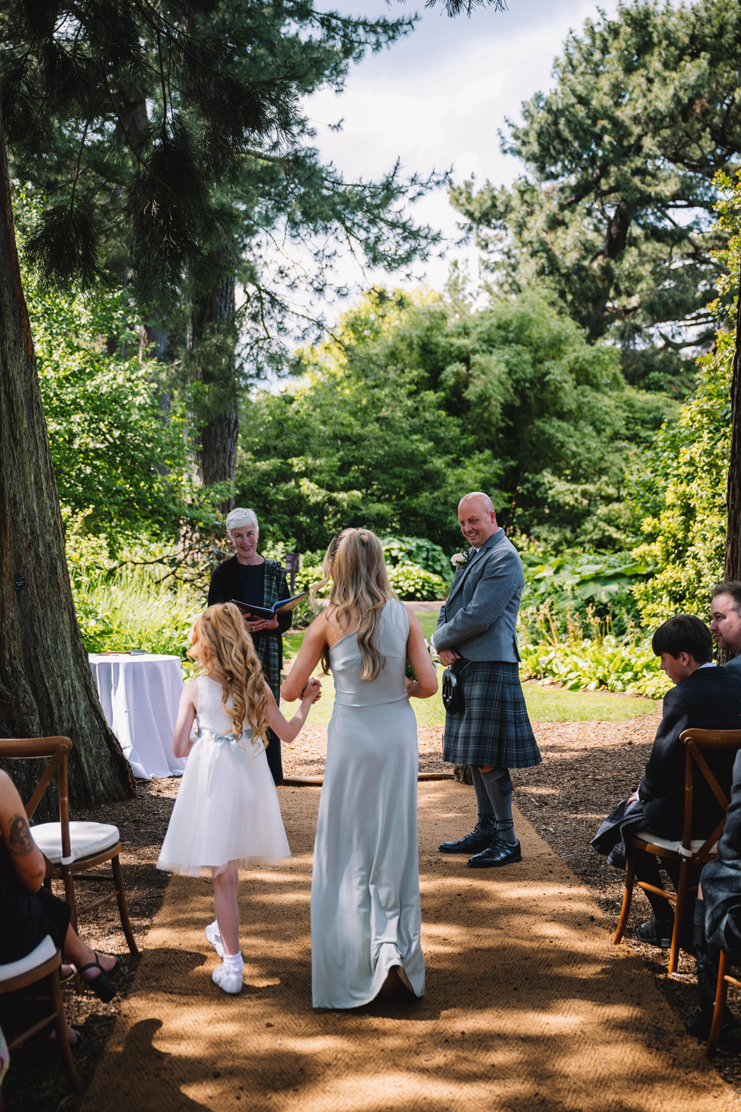 Couple standing with officiant during ceremony under trees.