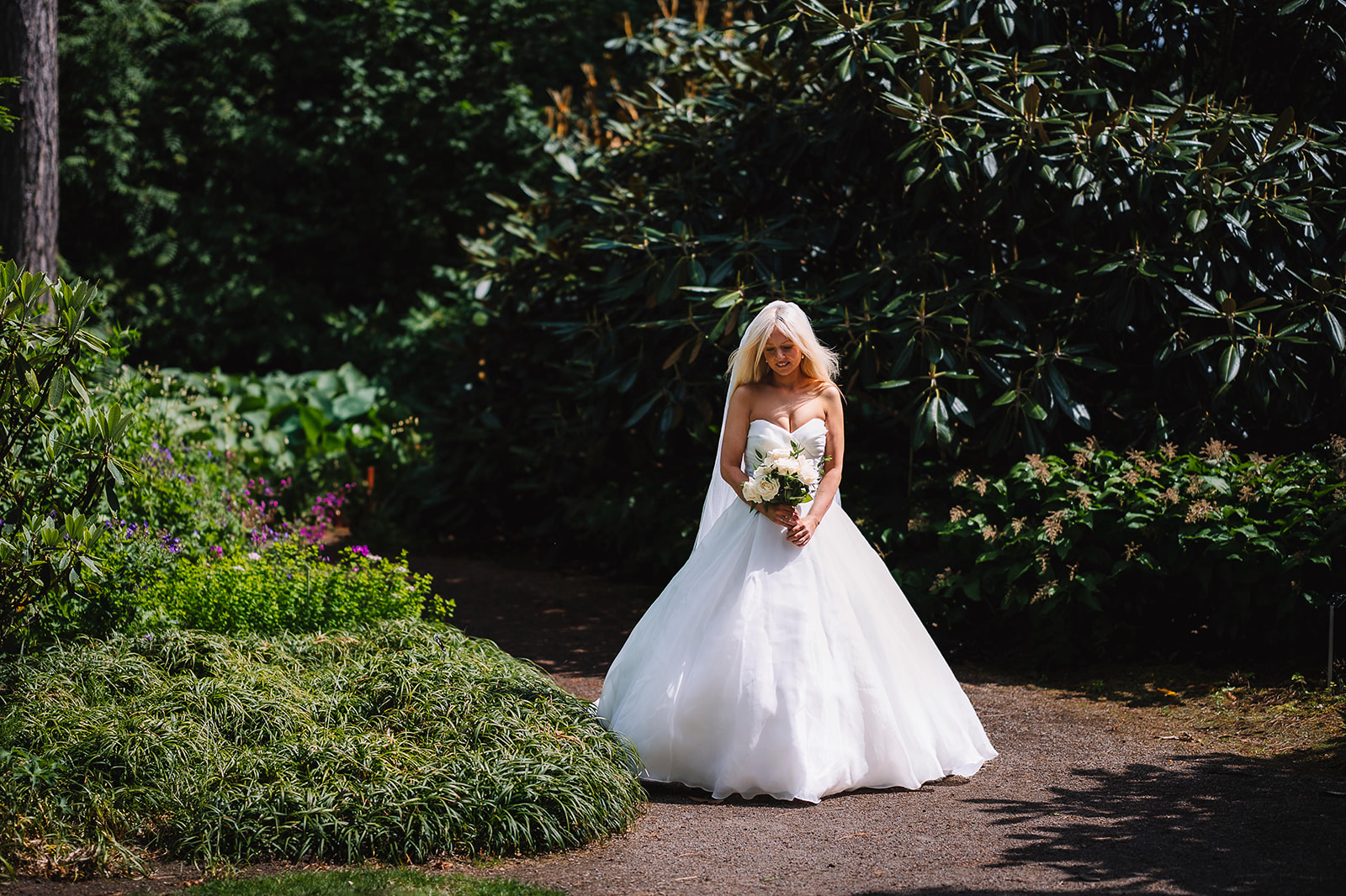 Bride standing alone holding bouquet in lush garden setting.