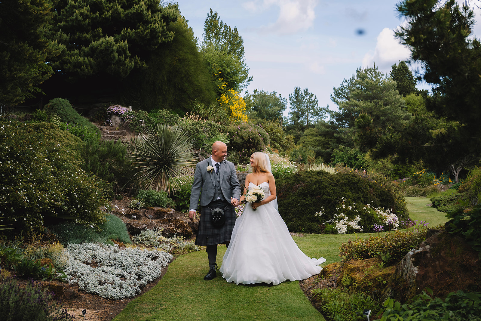 Couple standing together in landscaped garden after wedding ceremony.