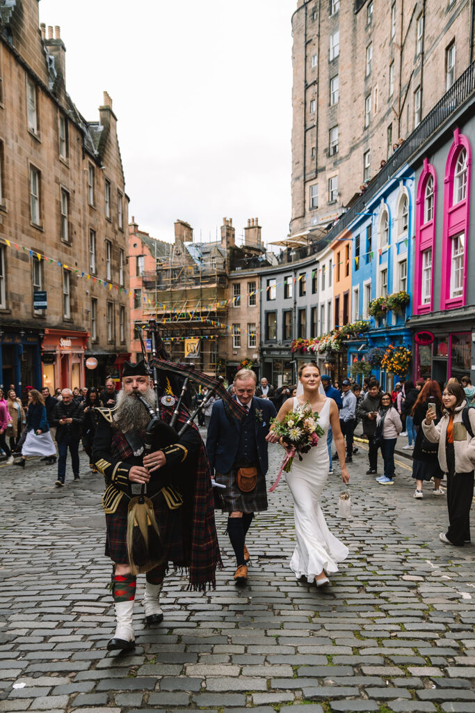 bride and father walk up Victoria Street led by piper