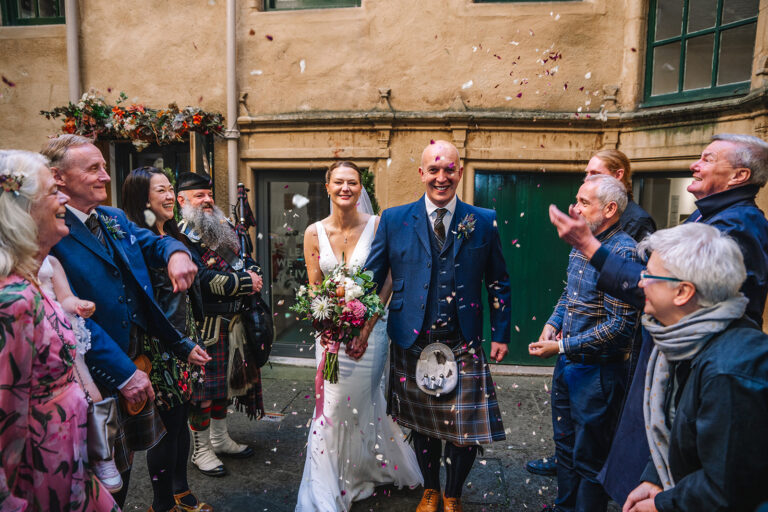 Bride and groom celebrating with guests outside historic building.