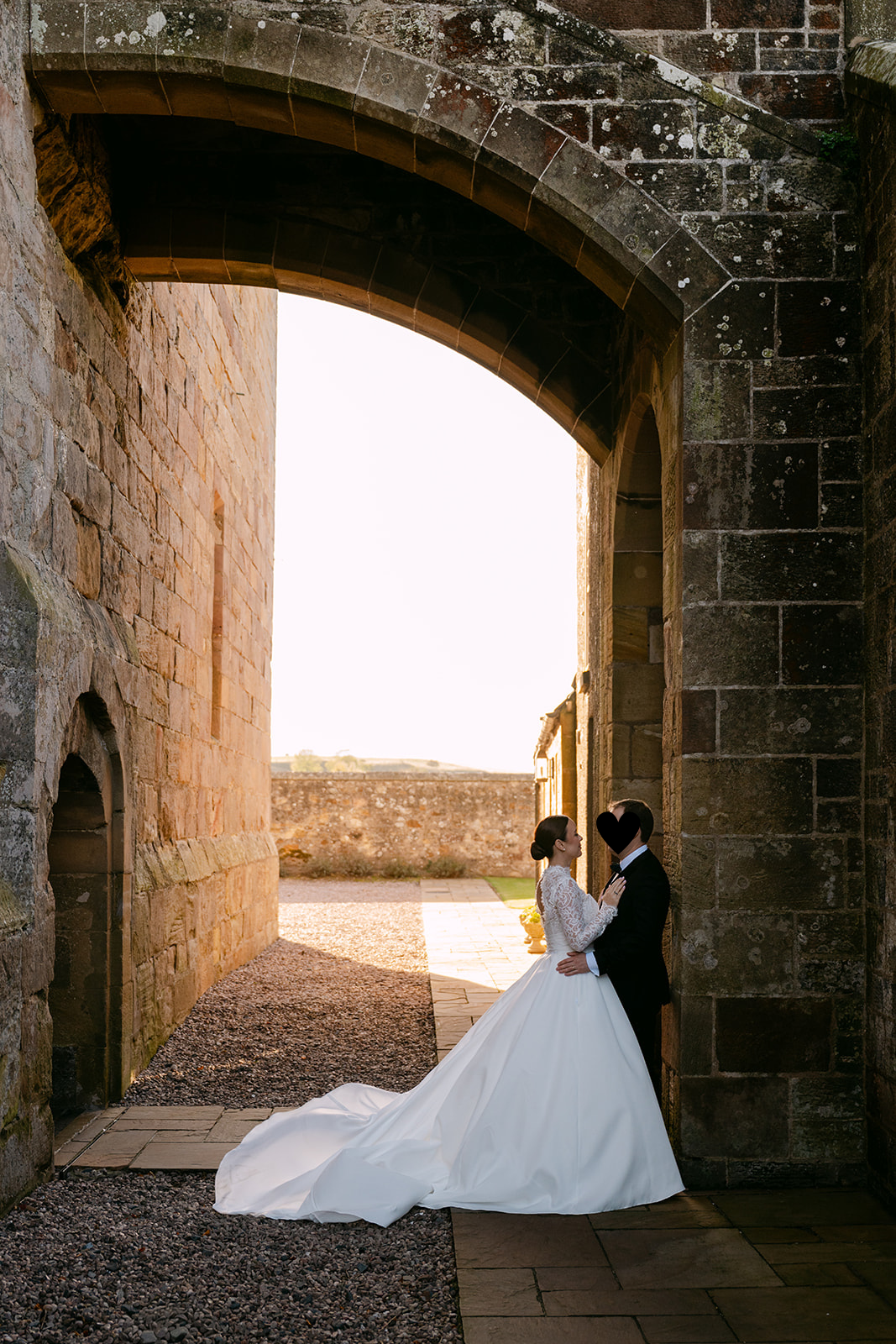 Bride and groom standing under archway with warm sunset light.