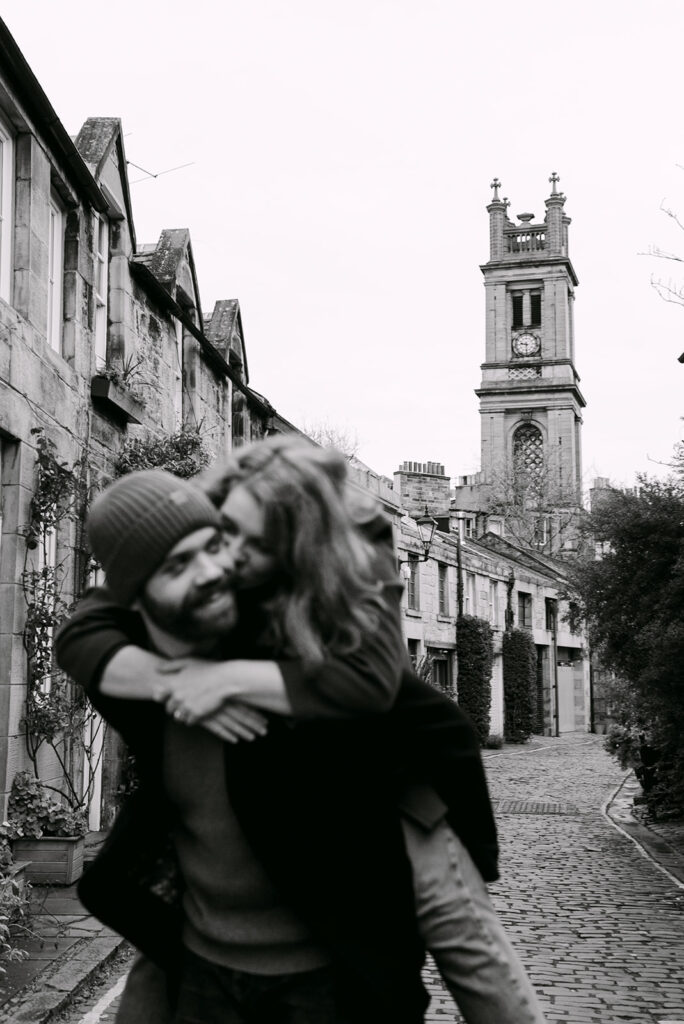 couple piggyback rides playfully on circus lane in edinbuRgh