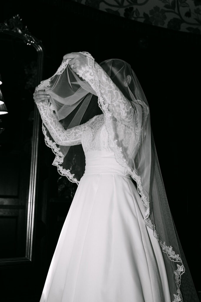 Bride lifting veil in black and white during bridal portrait.