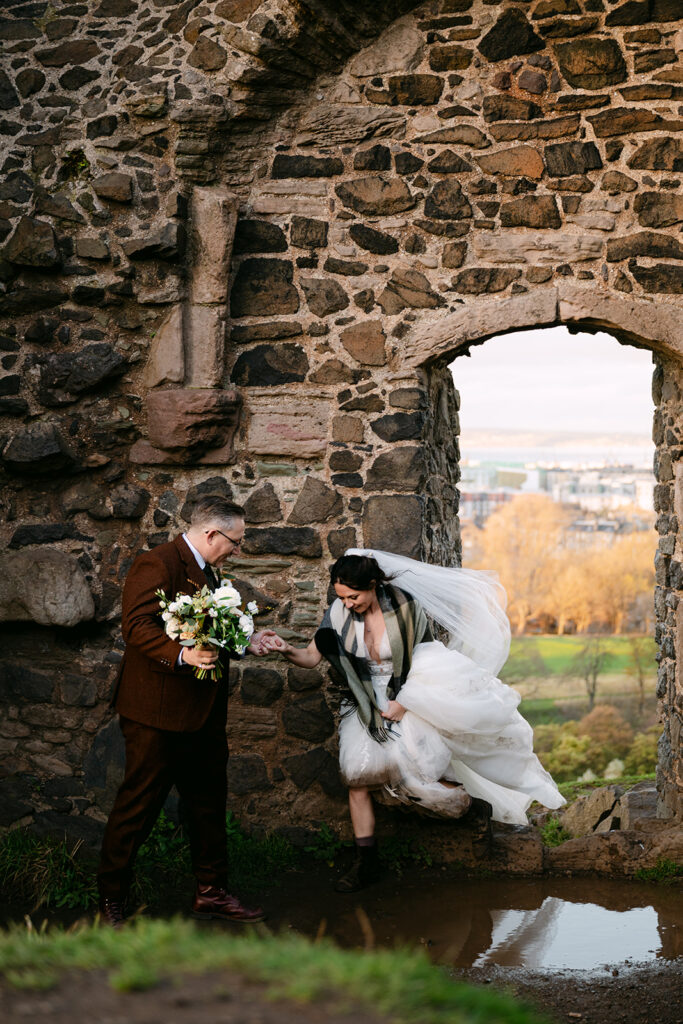 couple holding hands as bride walks through pond