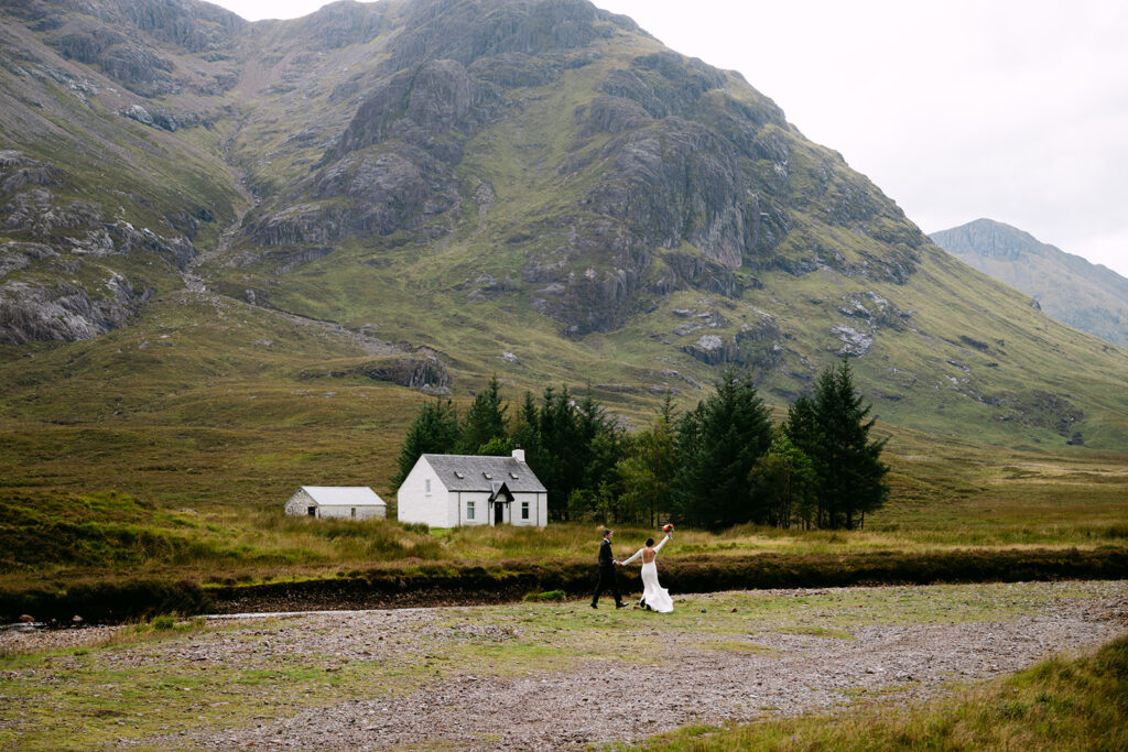Bride walking toward groom during elopement on grassy hill with panoramic glencoe view in background