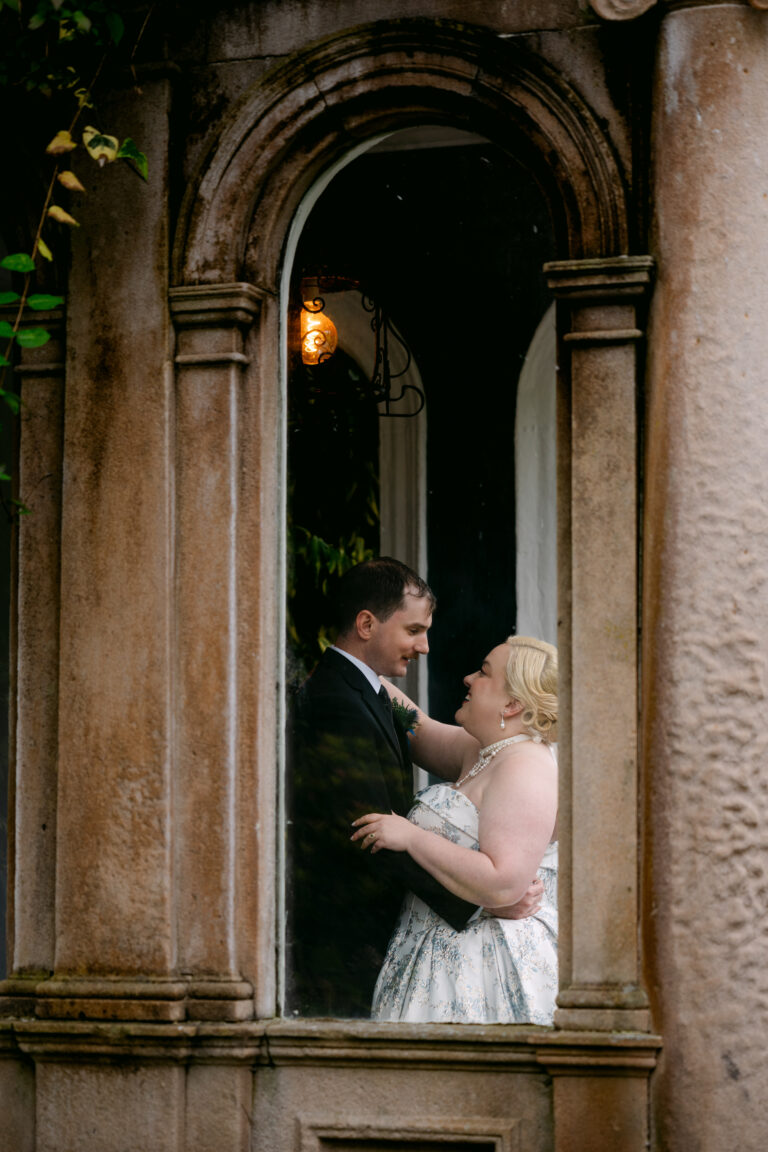 Bride and groom framed by an arched window at auchen castle